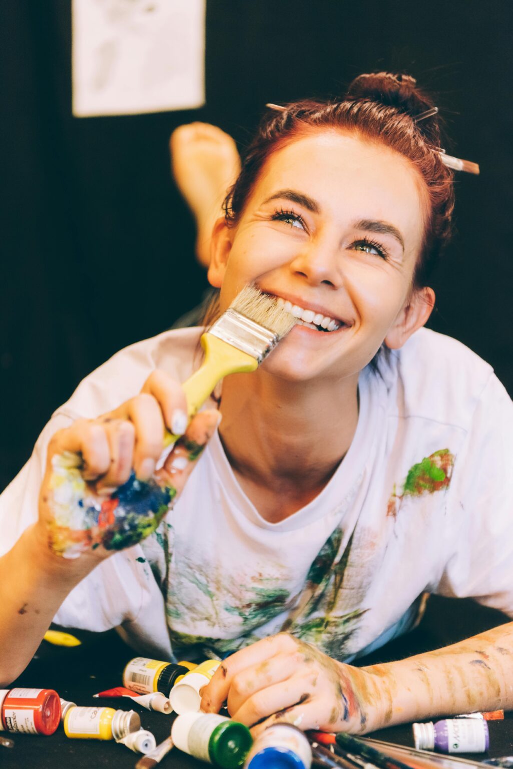 Smiling artist with paintbrush enjoying the creative painting process, surrounded by colorful paints.
