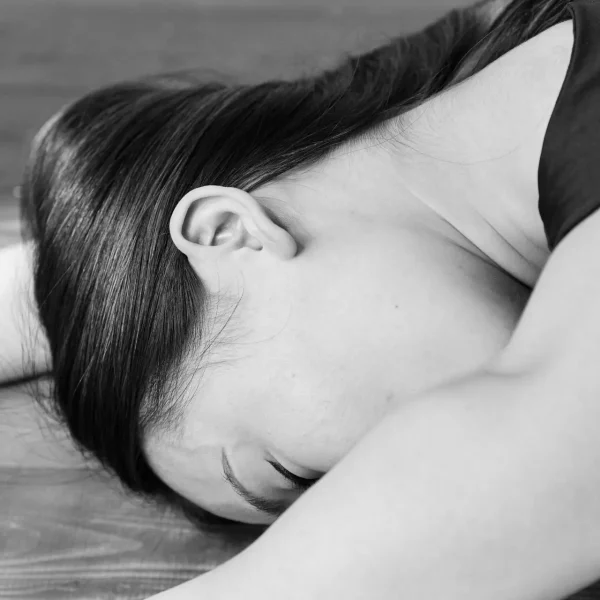 Woman lying on an exercise mat in a tranquil, black and white setting.